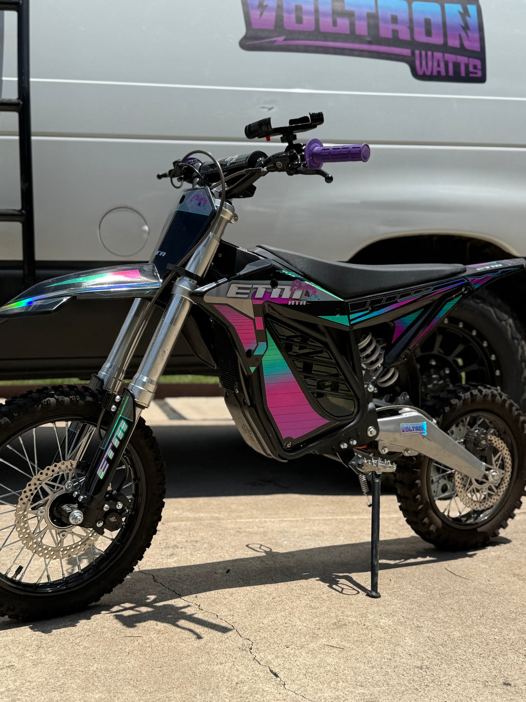 Motorcycle with colorful design parked in front of a white van with 'Voltron Watts' branding.
