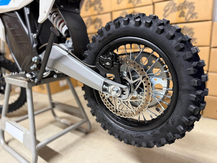 Close-up of a motorcycle wheel with knobby tire on a wooden floor.