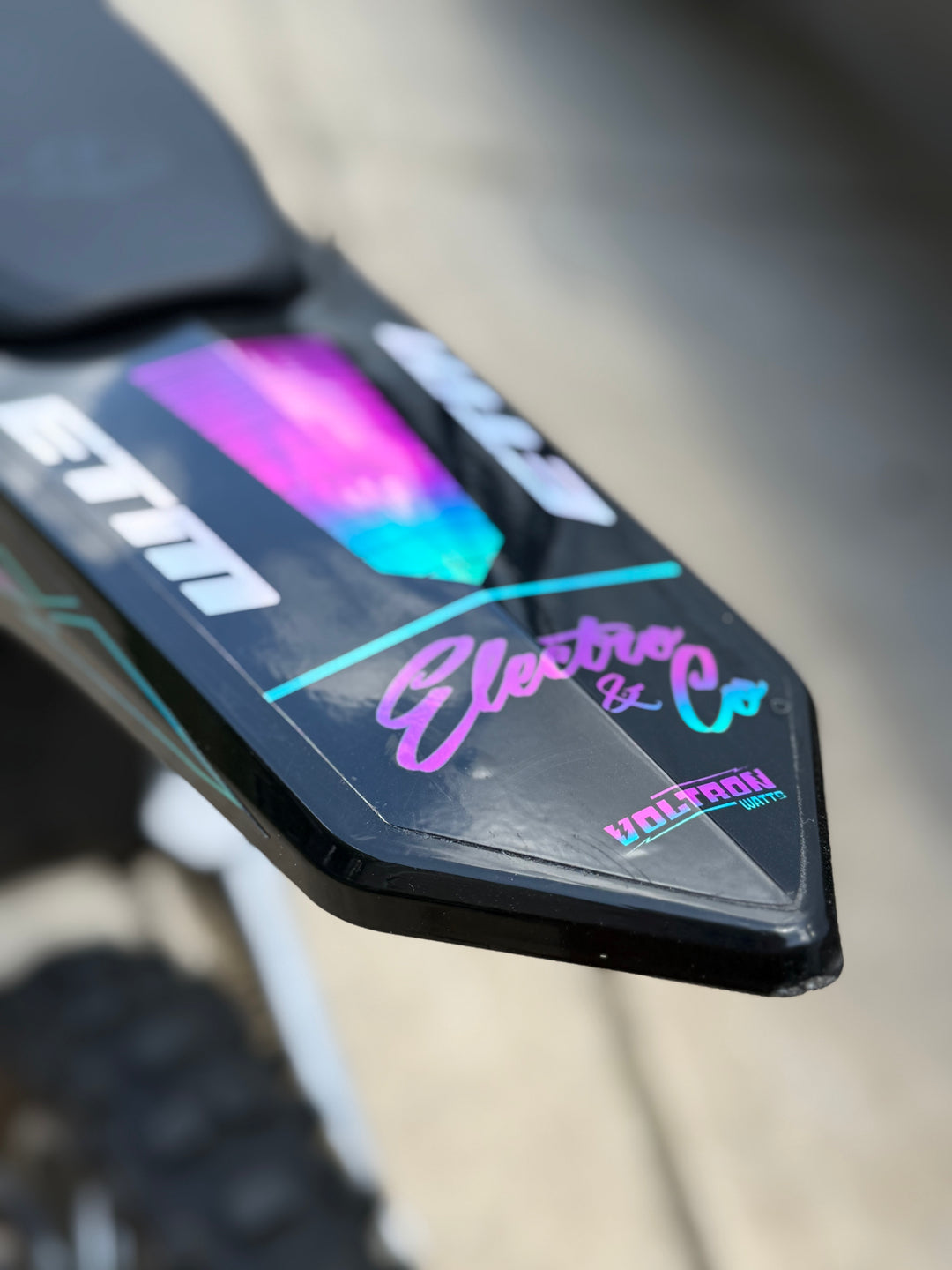 Close-up of a motorcycle mirror with colorful branding on a blurred background