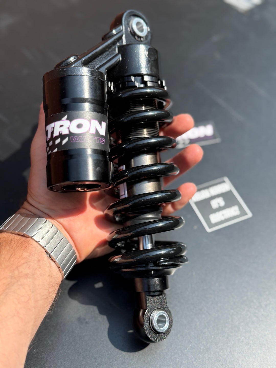 Hand holding a black shock absorber with 'VOLTRON' branding against a gray background