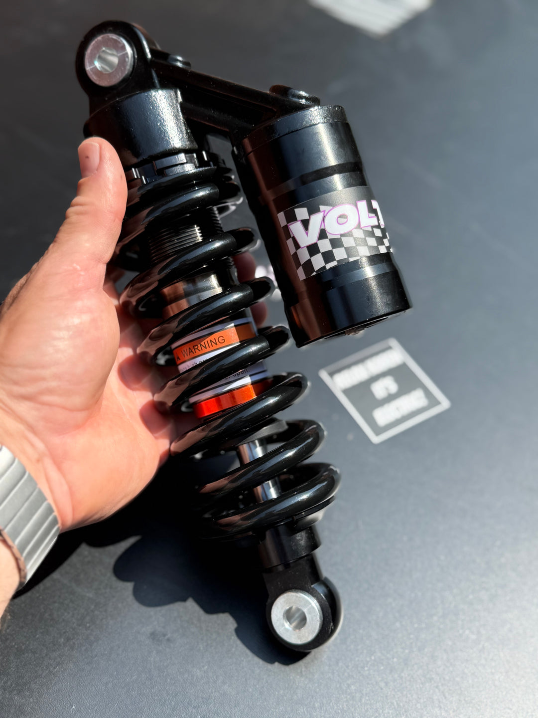 Hand holding a black shock absorber with 'Voltron' branding on a gray surface