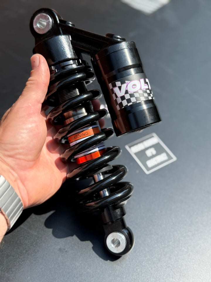 Hand holding a black shock absorber with 'Voltron' branding on a gray surface