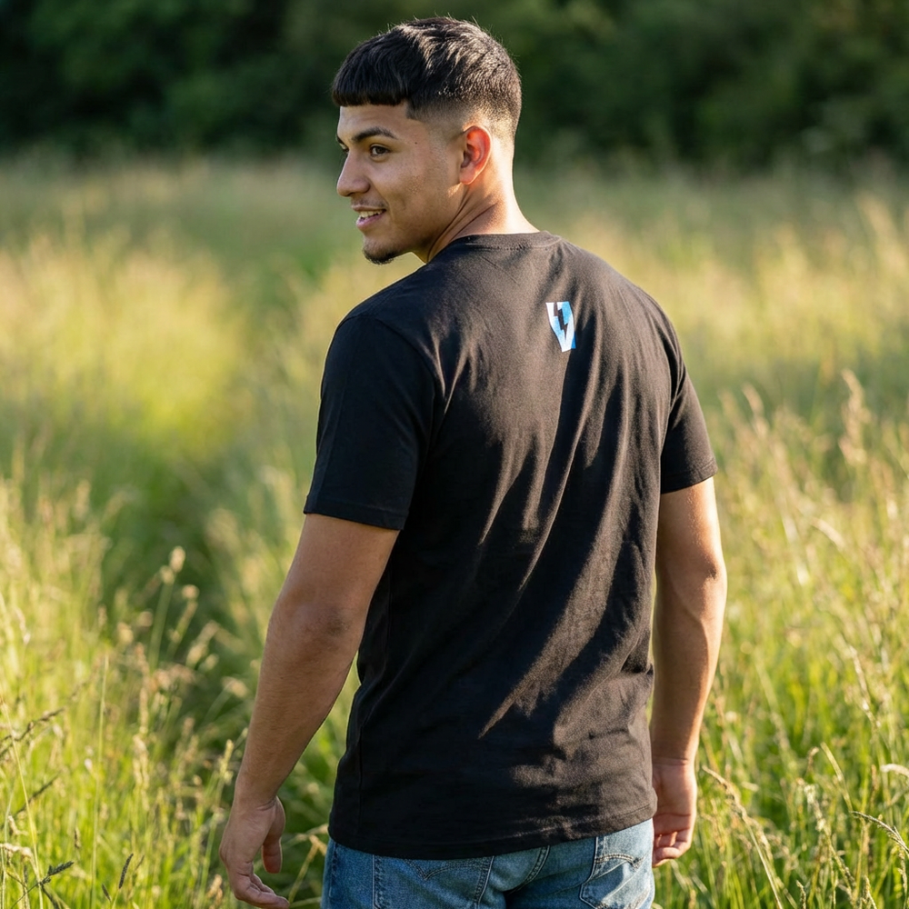 Man wearing a black t-shirt with a logo, standing in a grassy field.