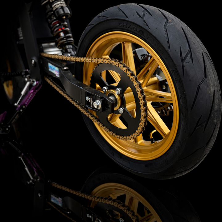 Close-up of a motorcycle wheel with gold rim and chain on a black background