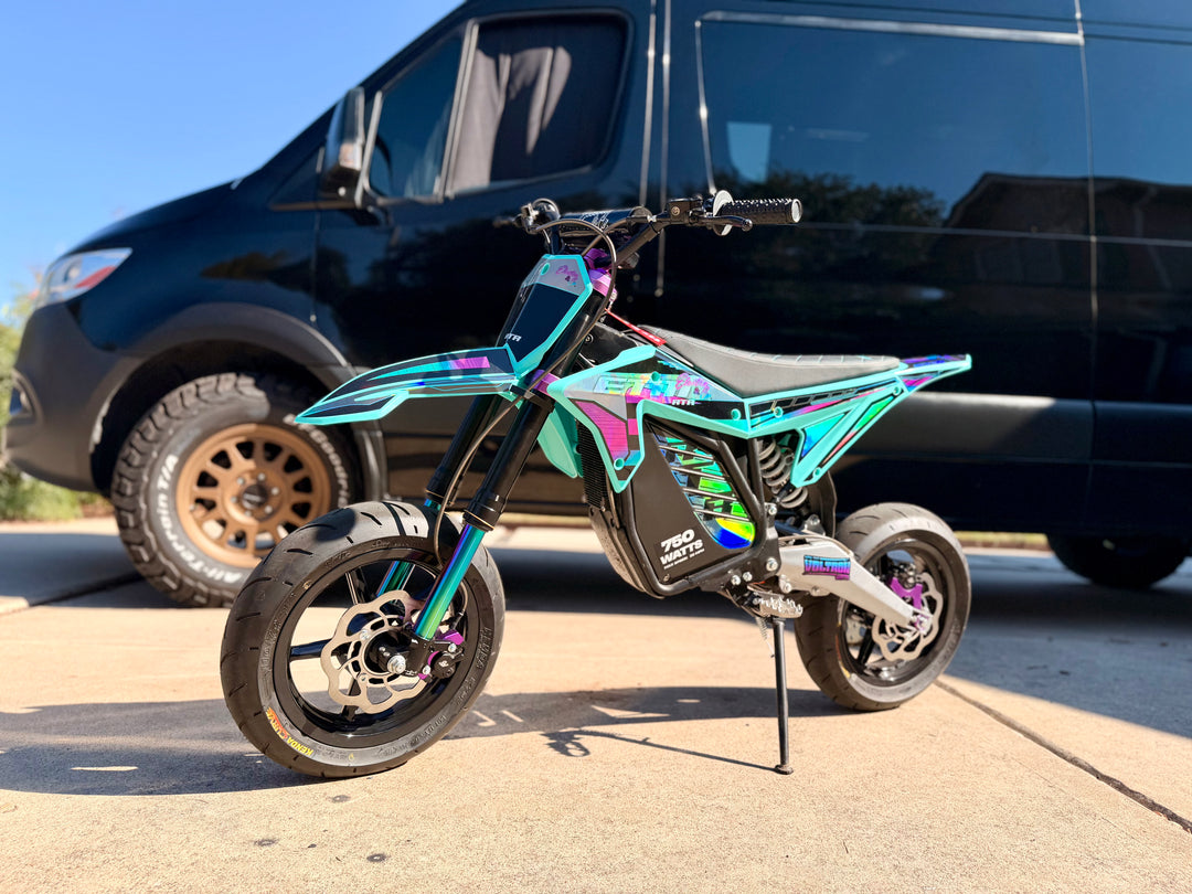 Colorful electric bike in front of a black van on a paved surface