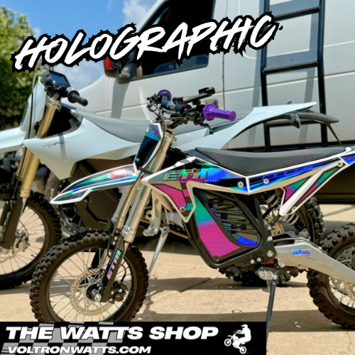 Motorcycle with holographic finish in front of a building, featuring 'The Watts Shop' branding.
