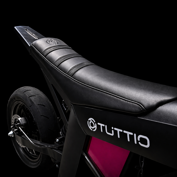 Close-up of a black scooter seat with 'Tuttio' branding on a black background