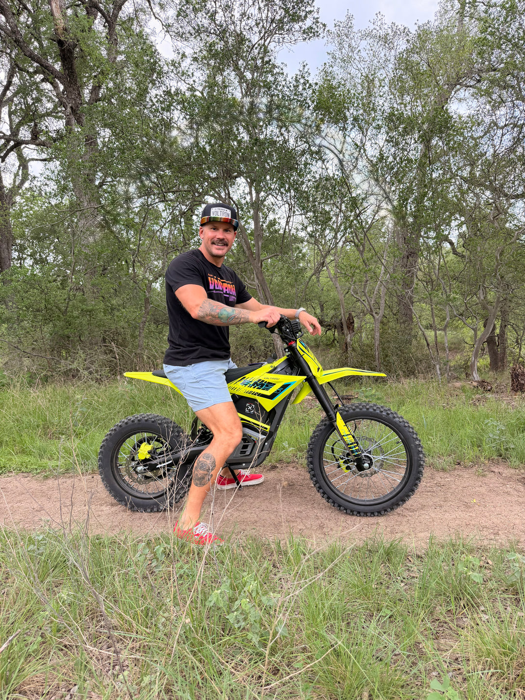 Man standing next to a yellow dirt bike on a trail with trees in the background