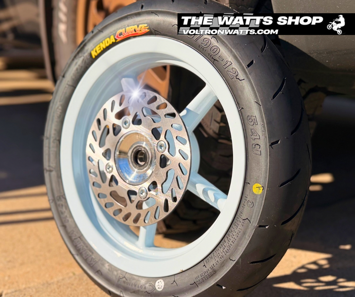 Close-up of a motorcycle wheel with Kenda Clevie tire and 'The Watts Shop' branding.