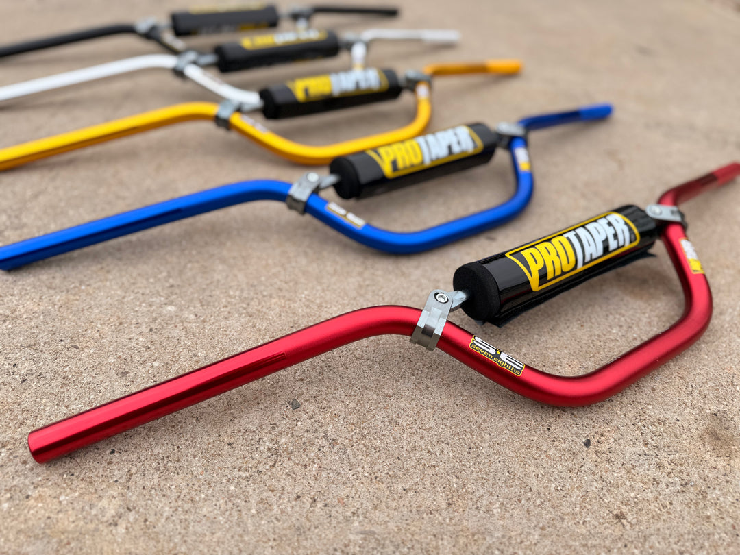 Set of colorful motorcycle handlebars with 'Pro Taper' branding on a concrete surface.