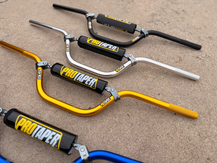 Four motorcycle handlebars with ProTaper grips on a concrete surface