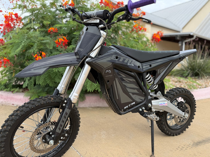 Black electric bike on a stand with a blurred background of greenery and a house.
