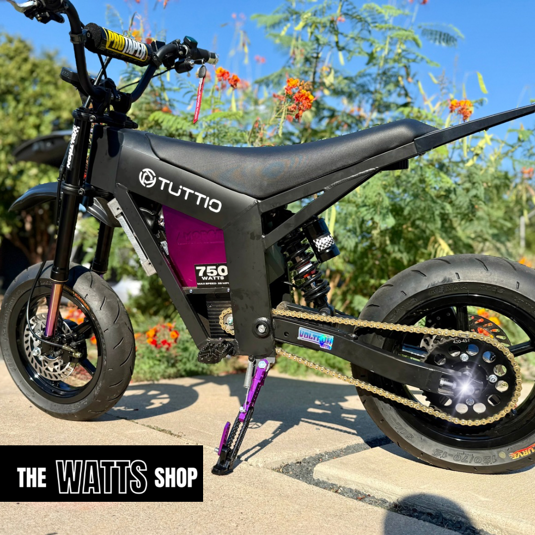 Black electric bike with 'Tuttio' branding on a sunny day with greenery in the background.