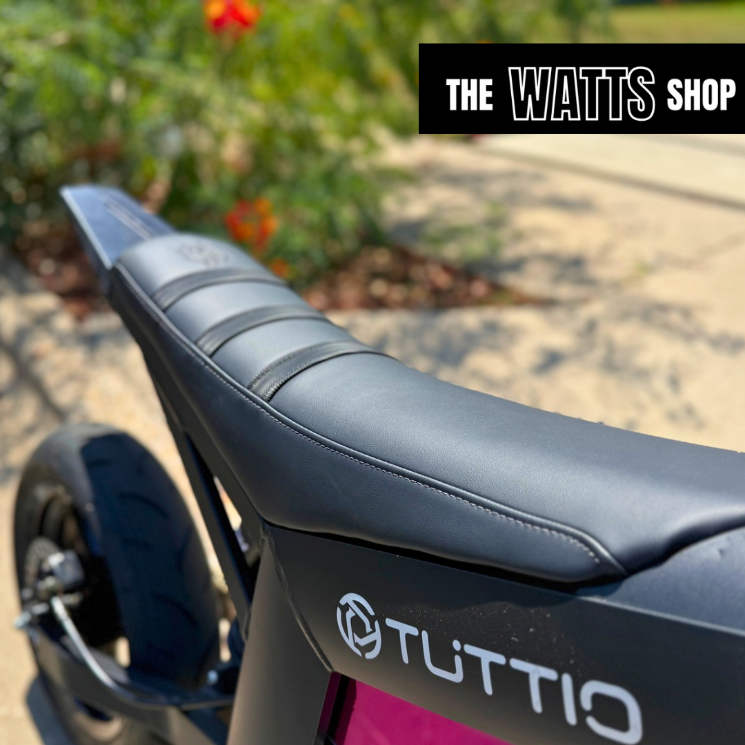Close-up of a motorcycle seat with 'Tuttio' branding, blurred natural background