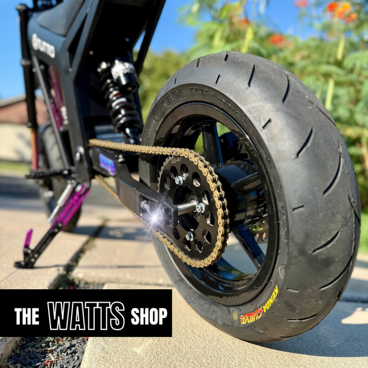 Close-up of a motorcycle tire with chain and 'The Watts Shop' branding.