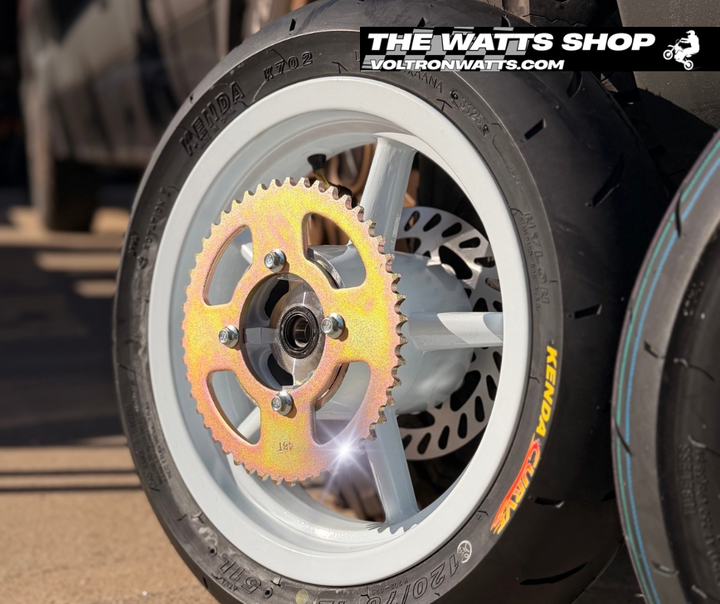 Close-up of a motorcycle wheel with a colorful sprocket, branded 'The Watts Shop'.